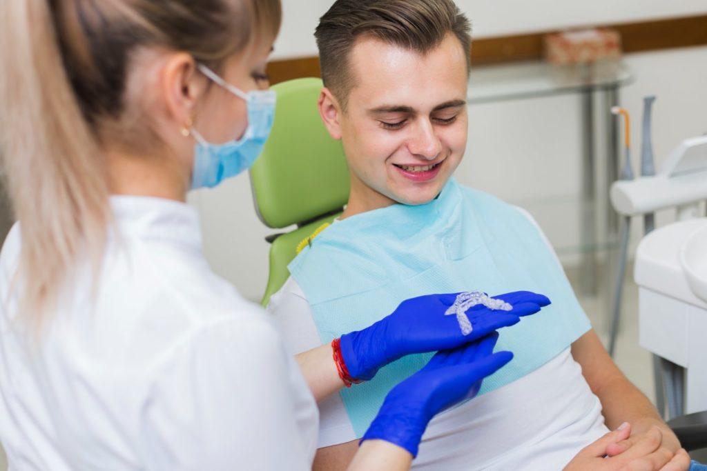 dentista mostrando un retenedor dental transparente a su paciente mientras explica como limpiar retendores dentales
