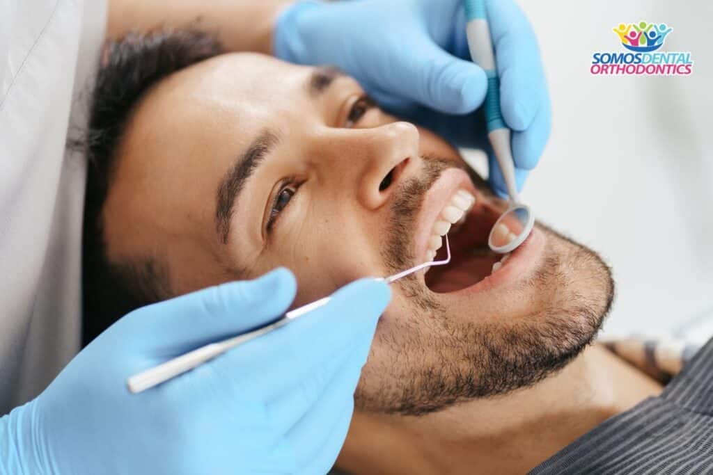 smiling young man sitting in dentist chair while doctor examining hi teeth and explaining what to eat after a root canal