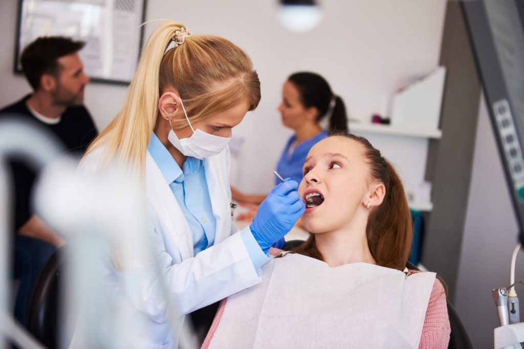 focused orthodontist using dental mirror and explaining why do people need braces