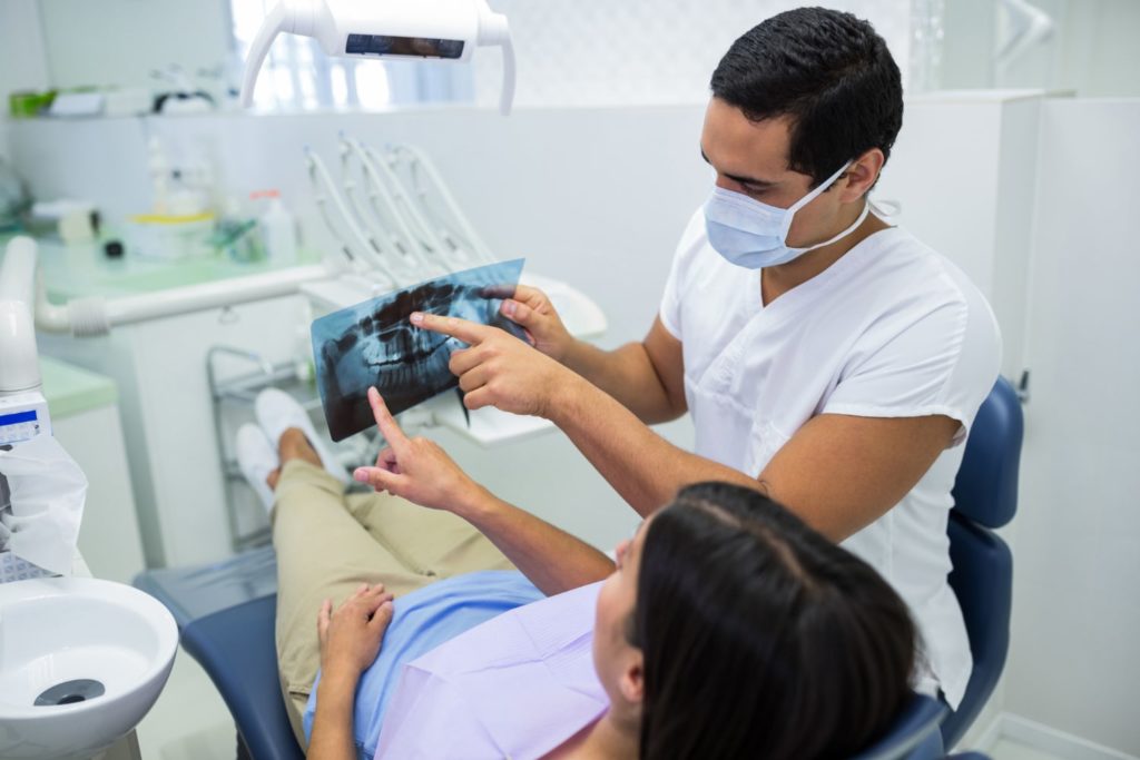 young male dentist examining x ray with the female patient recommending wisdom teeth removal recovery tips