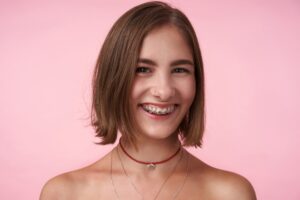 Young latin woman with short hair and braces in front of a pink wall happy to know how much do braces cost monthly