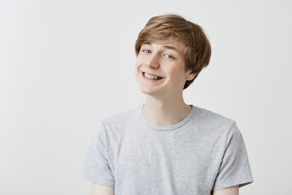 young and happy man smiling with braces in front of a white wall happy to found braces 99 per month