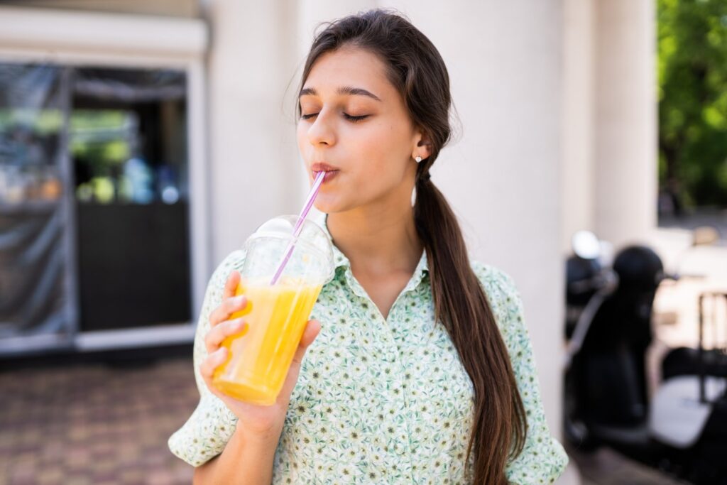 Young and happy Latin woman drinking a smoothie with a straw discovering what can you eat after getting braces