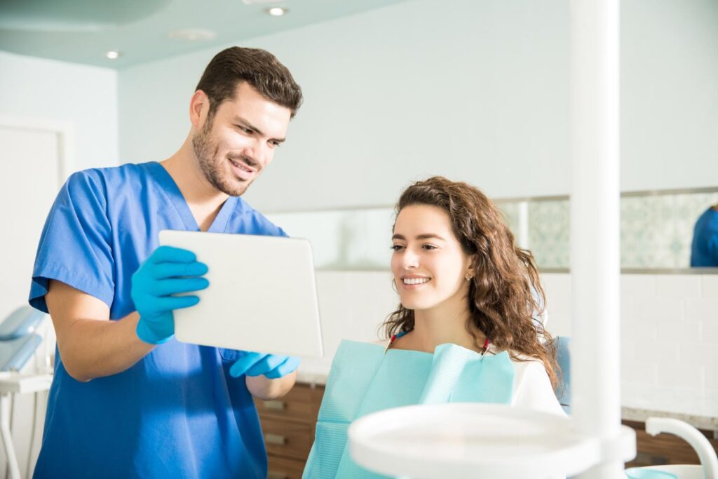 mid adult dentist showing digital tablet female patient during treatment dental clinic explaining the effects of not wearing a retainer after braces