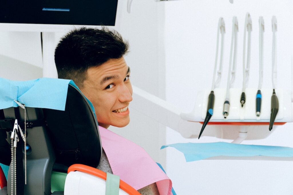 a young man in a dentist clinic sitting in a dentist chair smiling to the camera happy to know do you have to pay for an orthodontist consultation