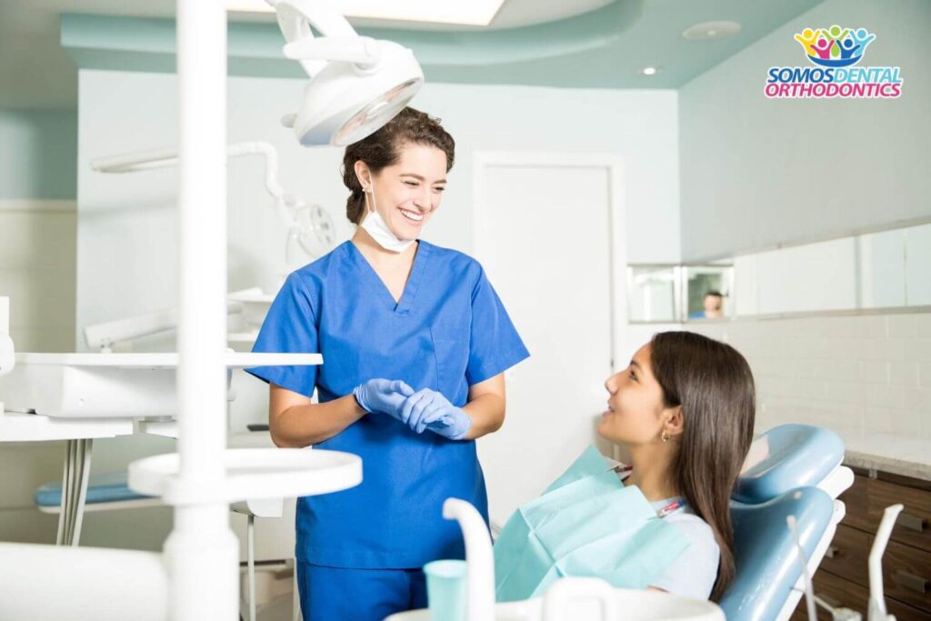 Smiling female dentist in uniform talking to teenage girl at dental clinic explaining how much does it cost to get braces in the United States