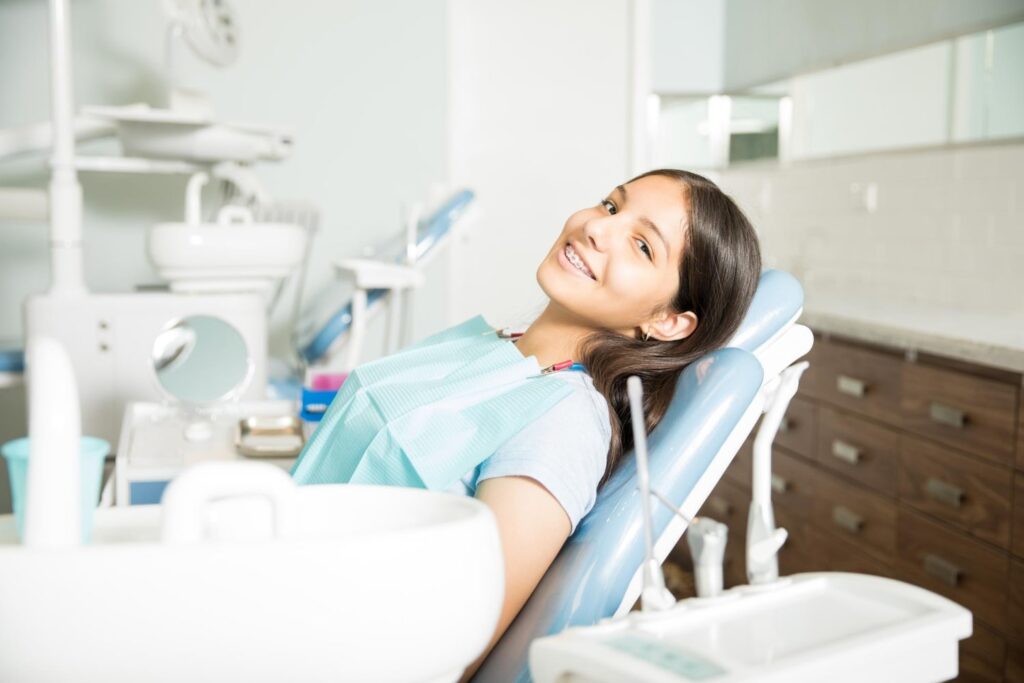 adolescente sonriente con frenos dentales sentada en la silla dental