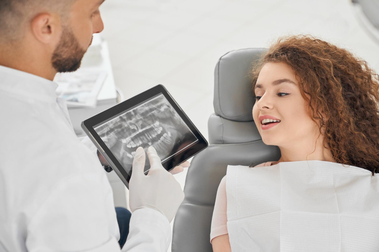 skilled male dentist showing x ray picture teeth to a woman to explain when do you need a crown