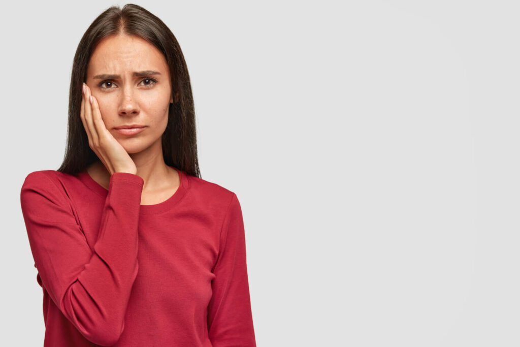 Indoor shot of sad unhappy European woman with unhappy expression keeps palm on cheek wondering are you awake during wisdom teeth removal