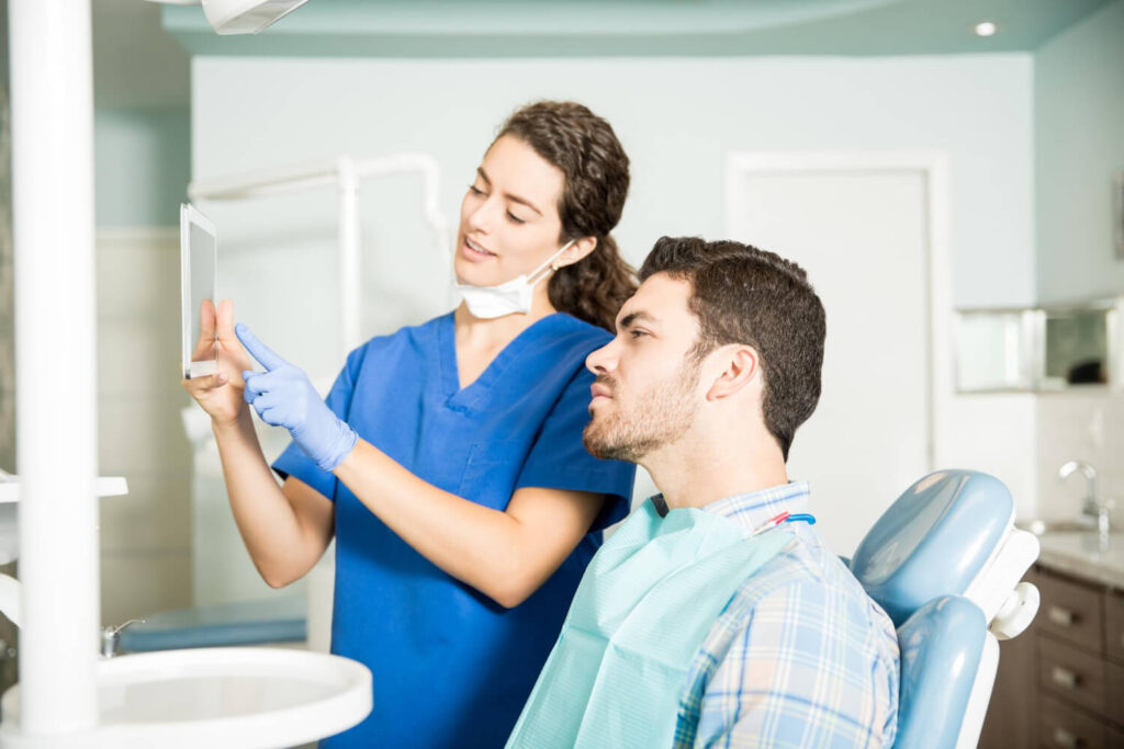 Young dentist showing digital tablet to male patient during treatment in dental clinic explaining if can another orthodontist remove my braces