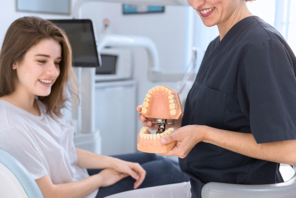 Close-up of a dentist showing teeth model to smiling patient explaining what to do when a dental crown falls out