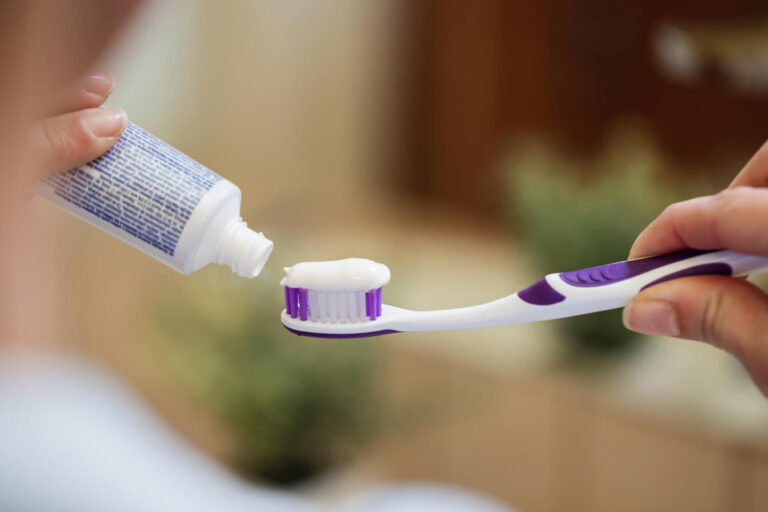 Closeup of unrecognizable woman applying toothpaste on toothbrush in the bathroom