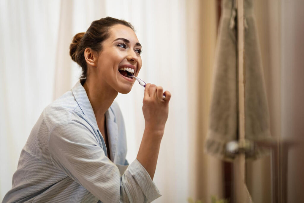 Happy woman cleaning her teeth with a toothbrush in the morning wondering if can I brush my teeth after wisdom teeth removal