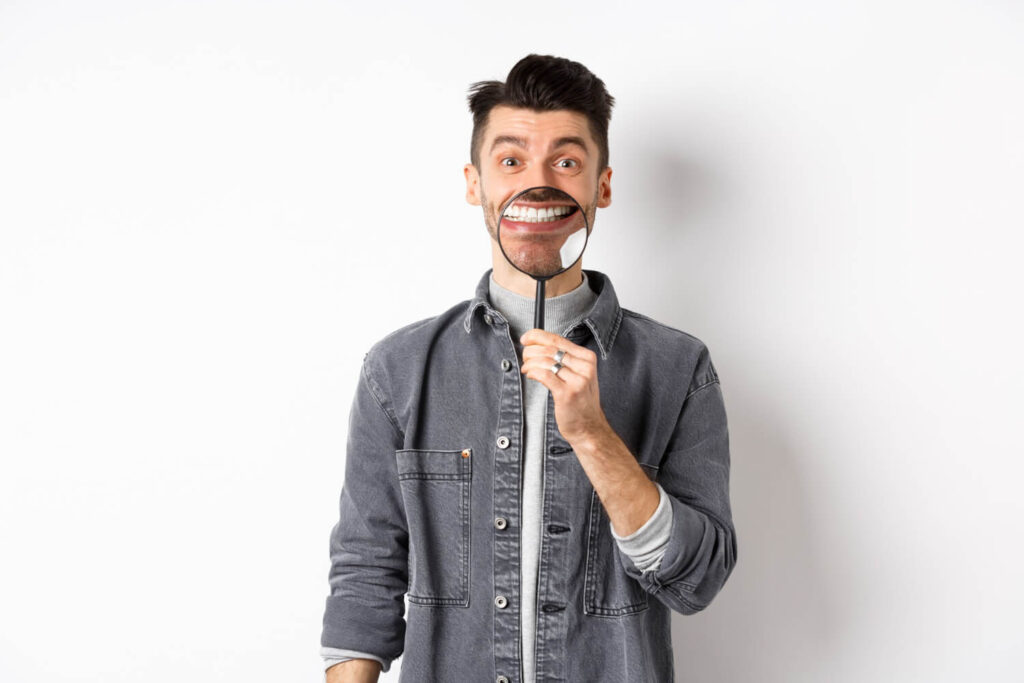 Handsome positive guy showing white perfect smile with magnifying glass