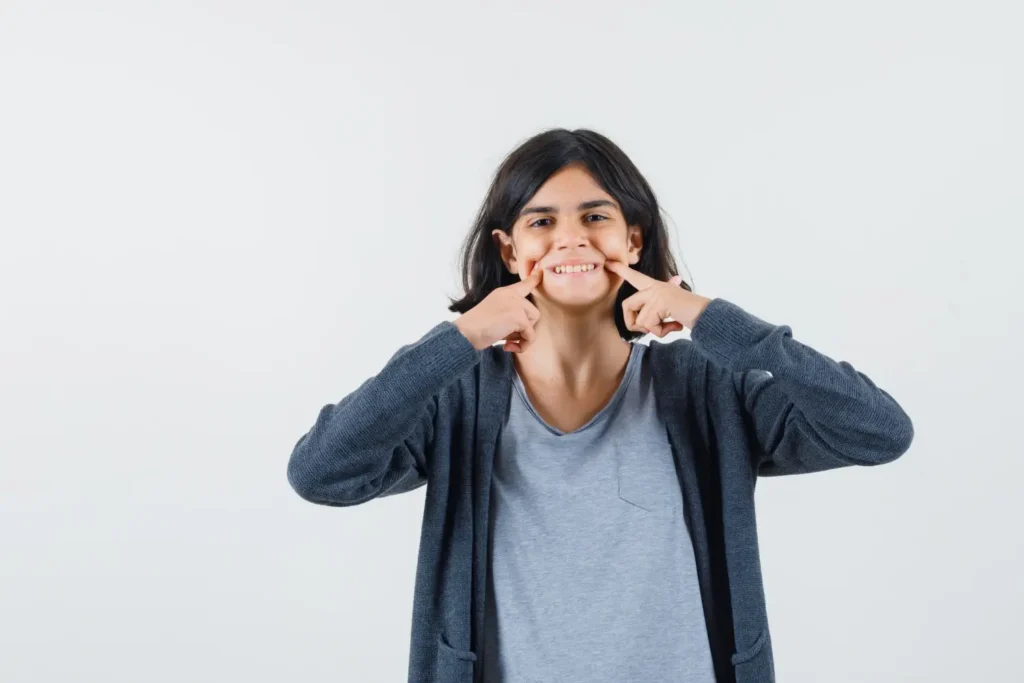 little girl keeping fingers on cheeks in tshirt jacket and looking cheery