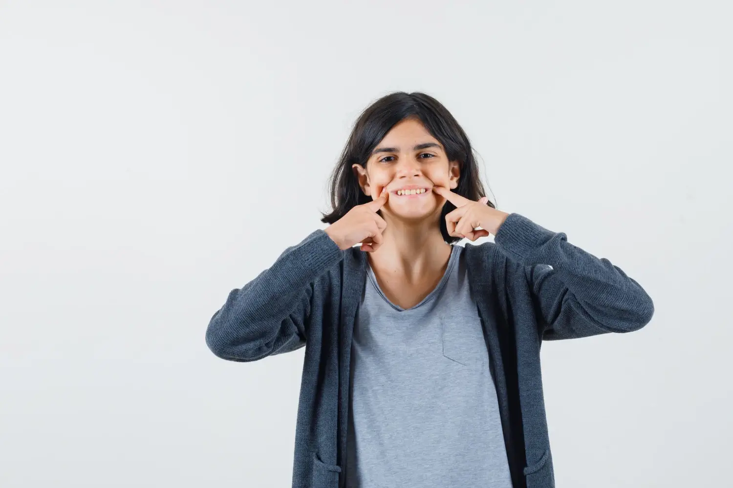 little girl keeping fingers on cheeks in tshirt jacket and looking cheery