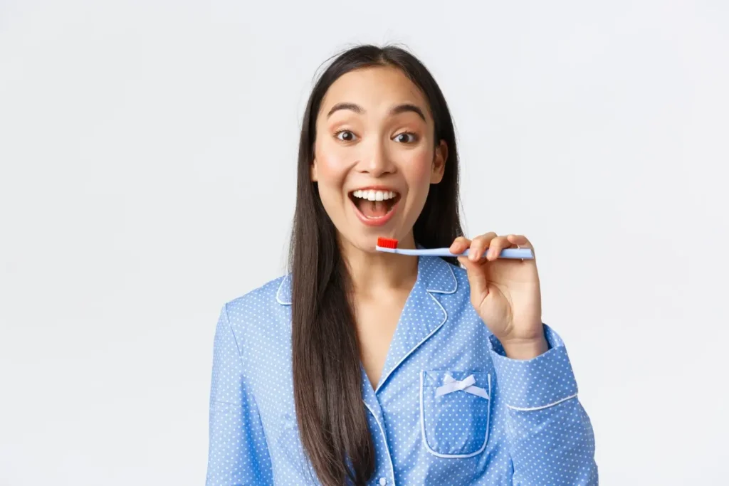 Cheerful pretty young hispanic girl in blue pajama brushing teeth