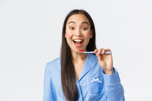 Cheerful pretty young hispanic girl in blue pajama brushing teeth